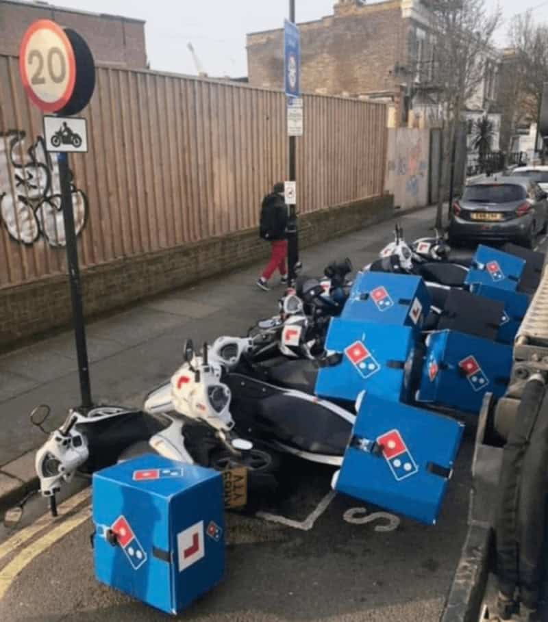 Multiple fallen Domino's pizza boxes and bikes on a street with a person walking by.