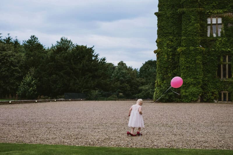 Child in pink dress holding a pink balloon outside a green ivy-covered building.