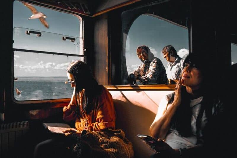 People on a train with a view of the sea and sky outside the window.