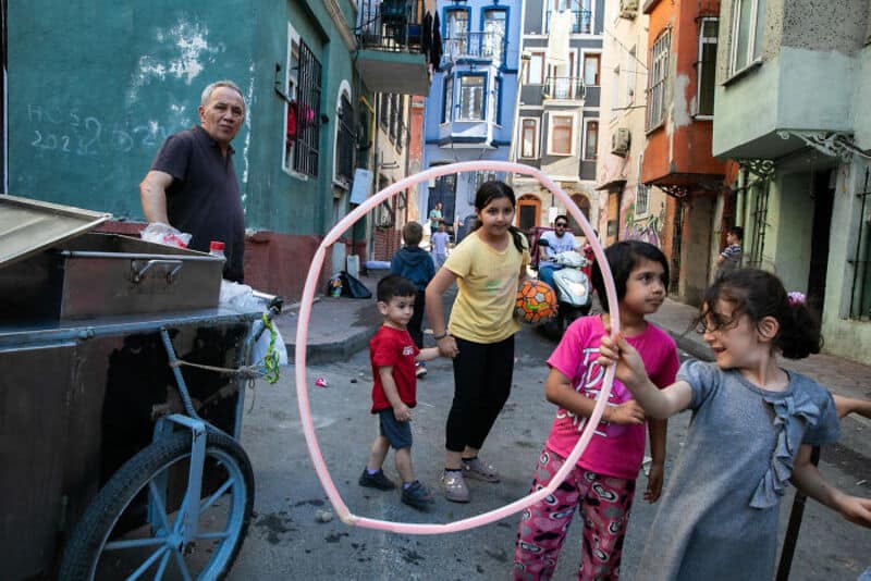 Children playing with a hula hoop in a colorful urban alleyway.