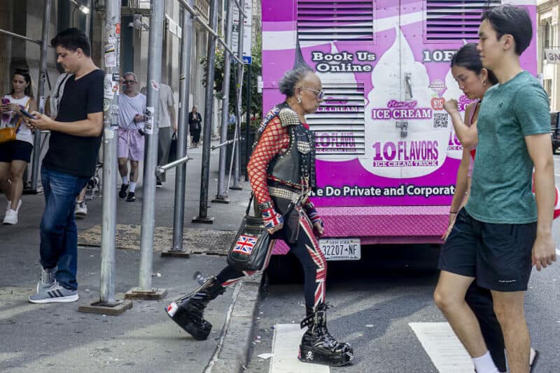 People walking on city street near ice cream truck and scaffolding.
