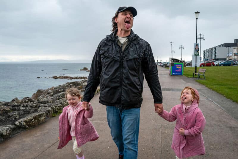Man walking with two young girls along a seaside promenade.