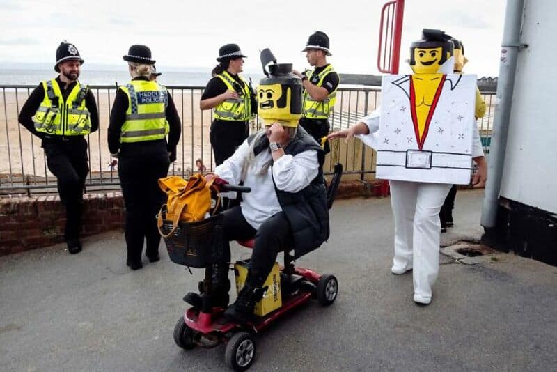 People in LEGO costumes and police officers on a waterfront promenade.
