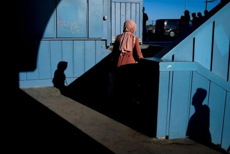 Woman with headscarf walking up blue stairs, shadows cast on wall and ground.