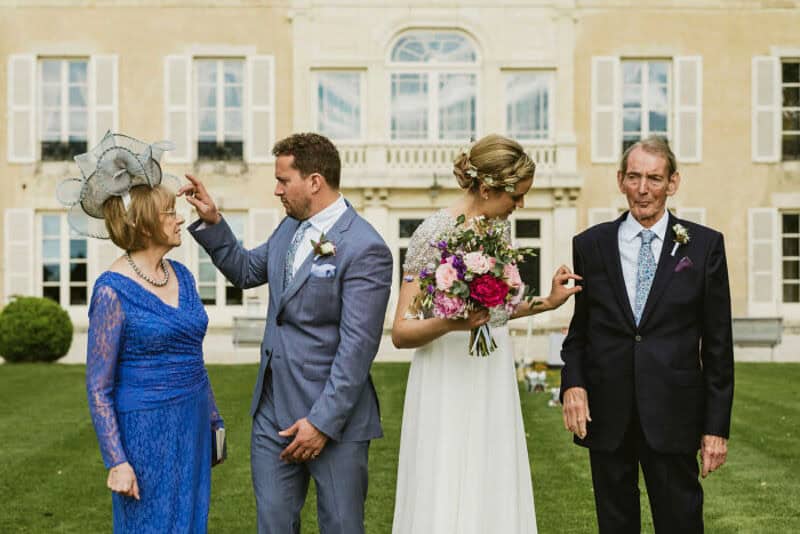 Wedding scene with four people outside a grand building, including a bride, groom, and two older on-.