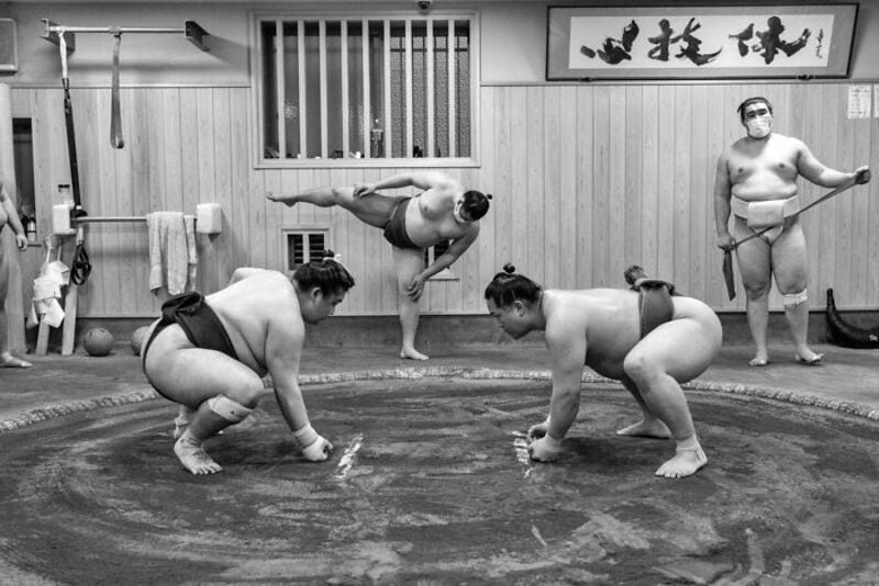 Sumo wrestlers practicing in a traditional dojo with a referee observing.