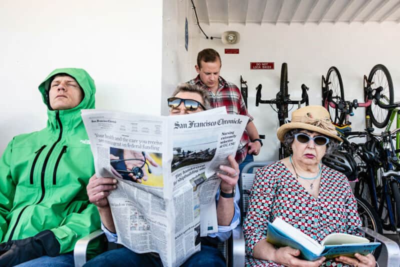 People sitting on a bench, reading and relaxing in a bike parking area.