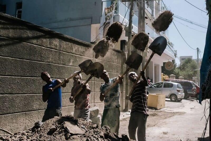 People throwing dirt and debris with shovels in an urban setting.