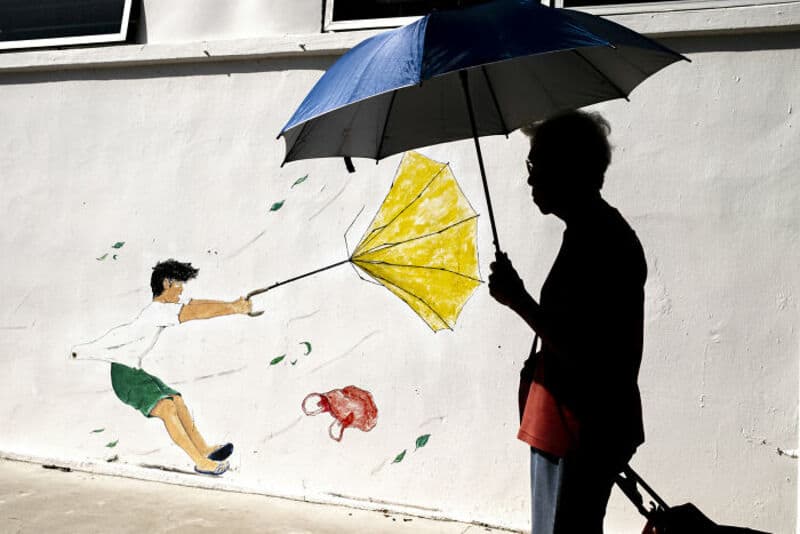 Child pulling an umbrella with a mural of a boy flying a kite on the wall.