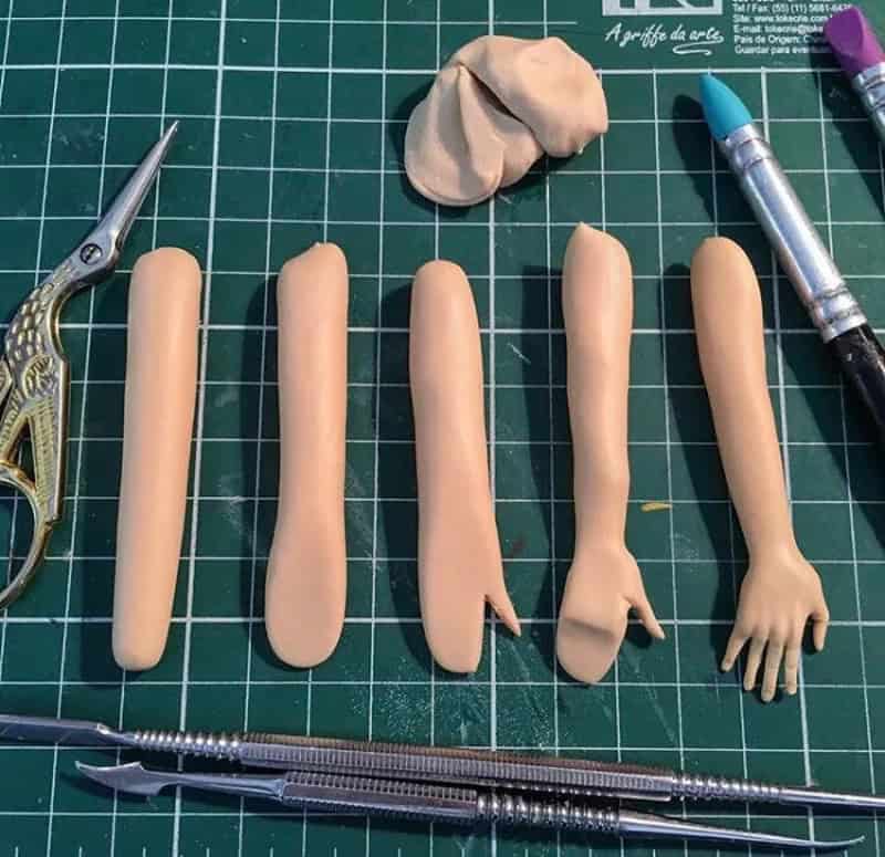 Five clay fingers with different shapes and a small clay hand on a green cutting mat.