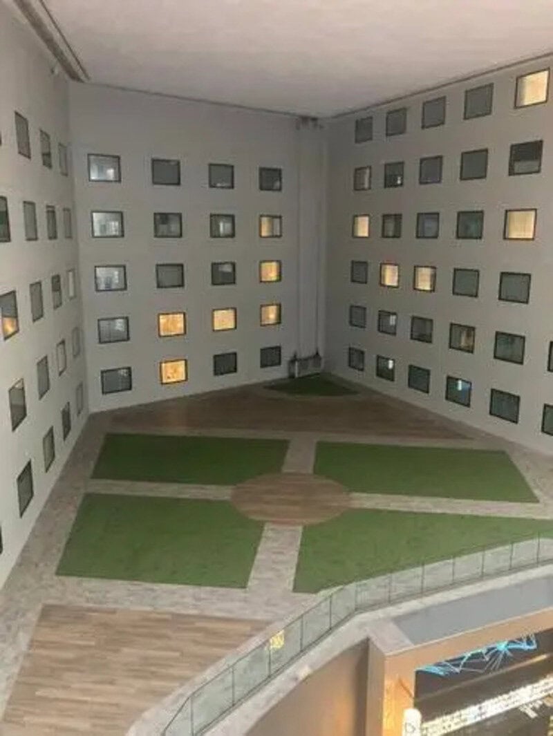Interior view of a courtyard with green grass and pathways, surrounded by a building with many small.