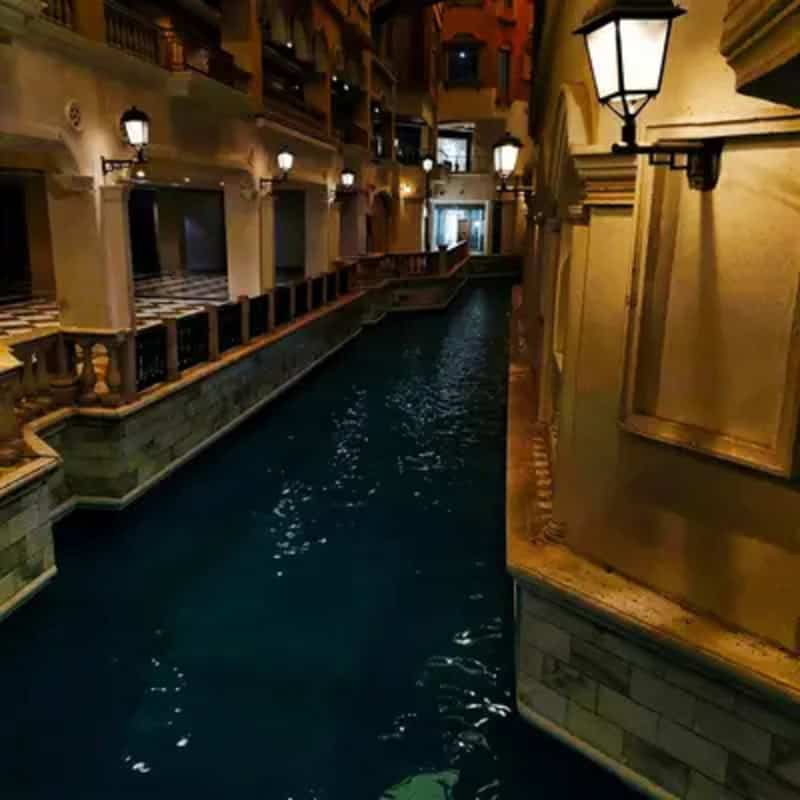 Indoor canal with warm lighting and balconies in a hotel or mall setting.