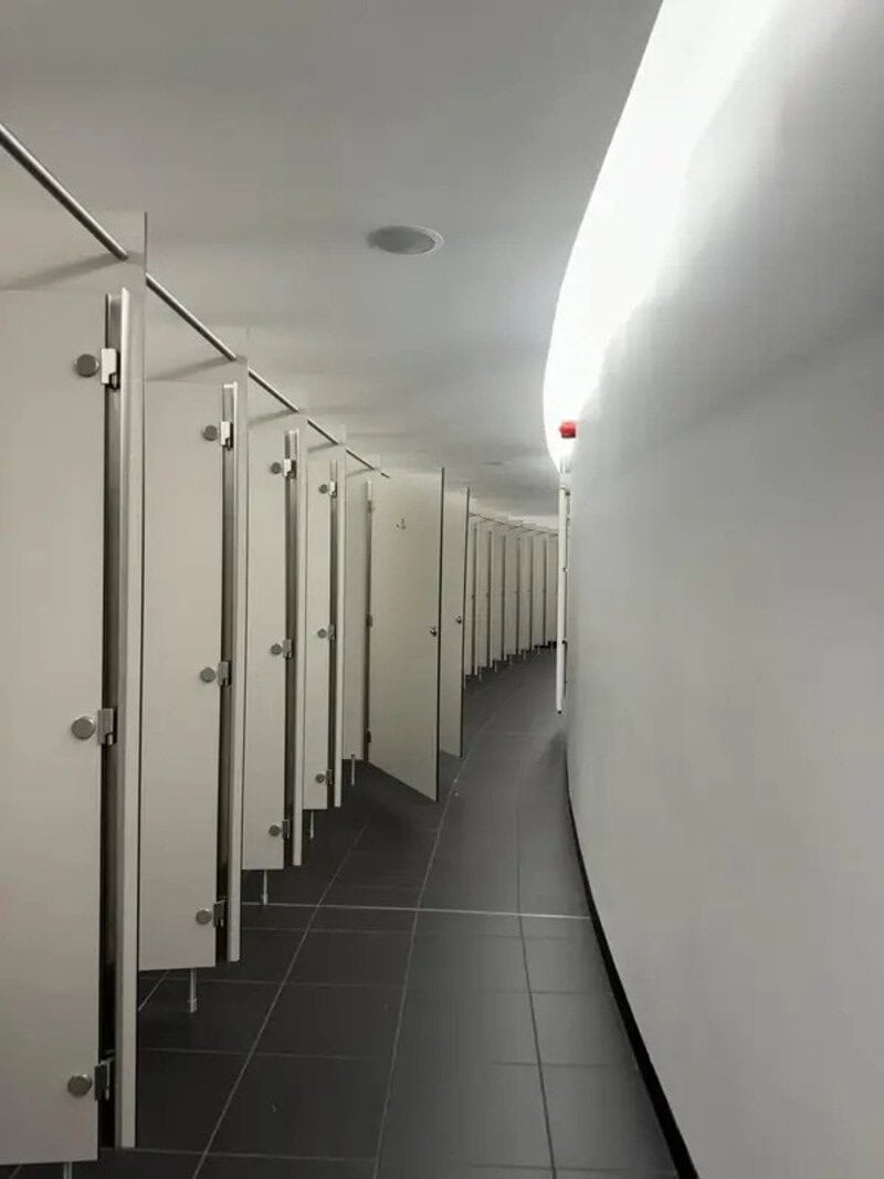 Empty public restroom with curved white wall and multiple stalls.