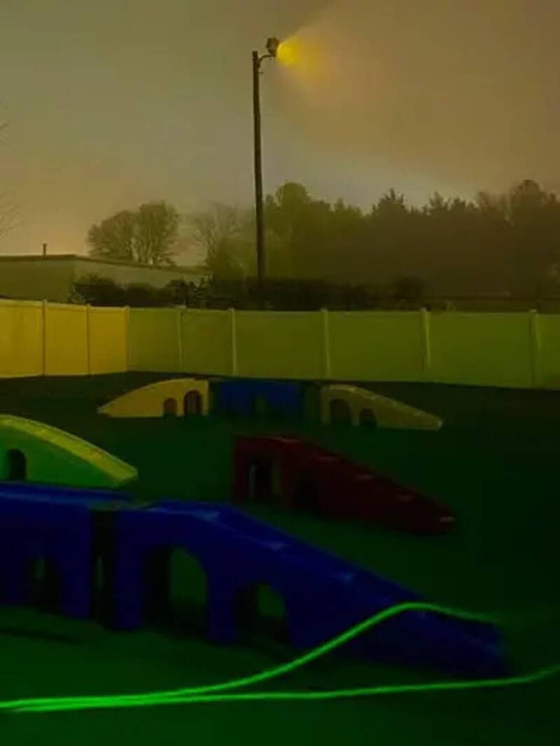 Playground with colorful slides under a streetlamp at dusk, surrounded by a fence.