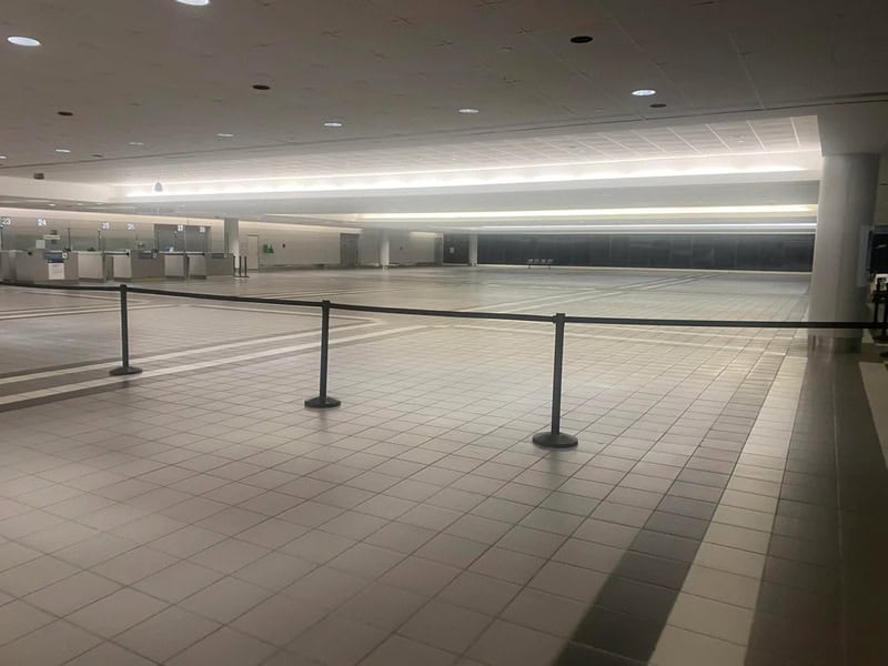 Empty airport terminal with barriers and minimal lighting.