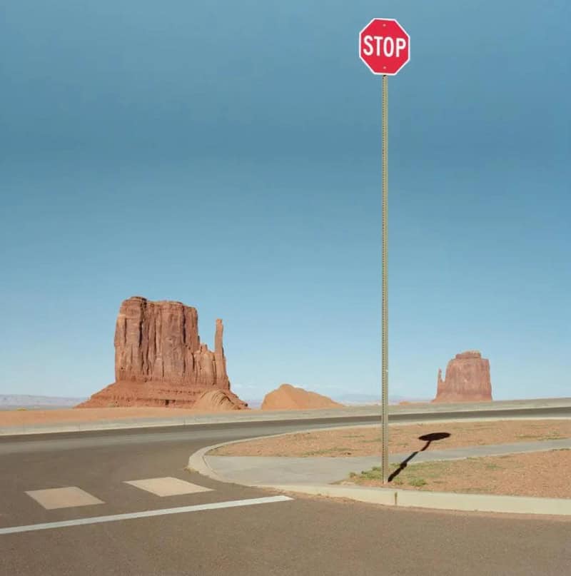 Stop sign in a desert landscape with rock formations and a clear blue sky.