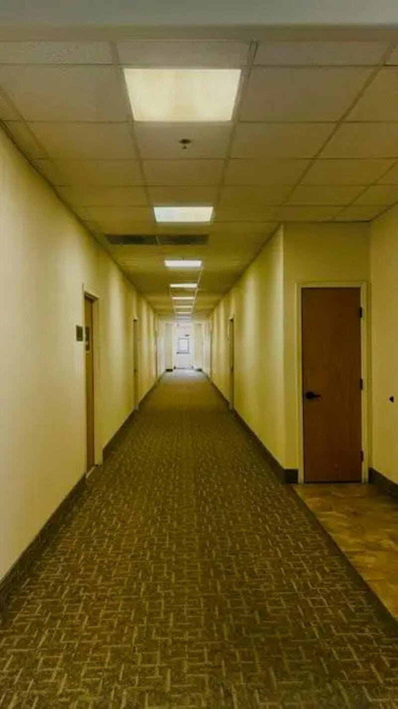 Long, empty corridor with closed doors and fluorescent ceiling lights.