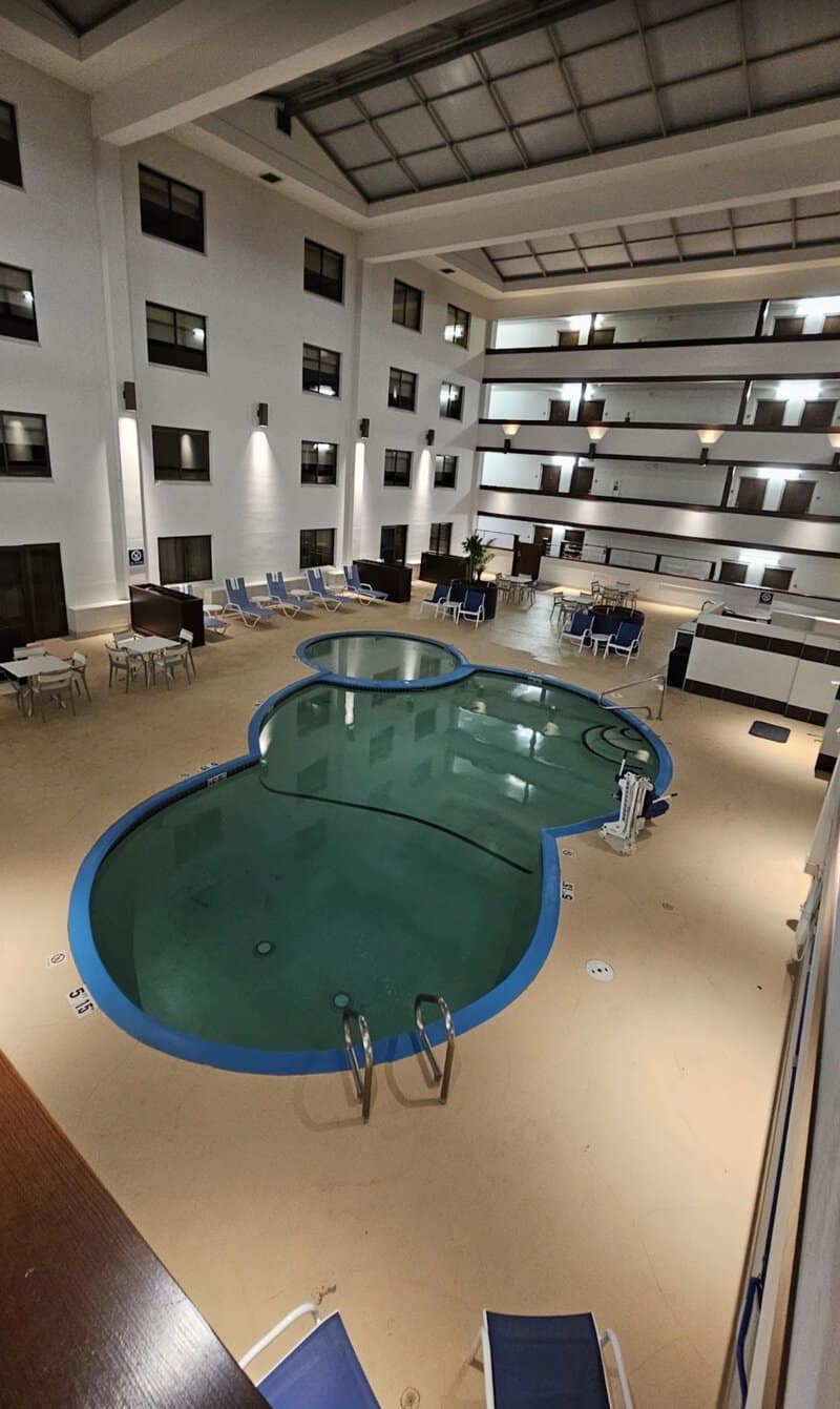 Indoor hotel pool with empty lounge chairs and multiple floors of rooms.