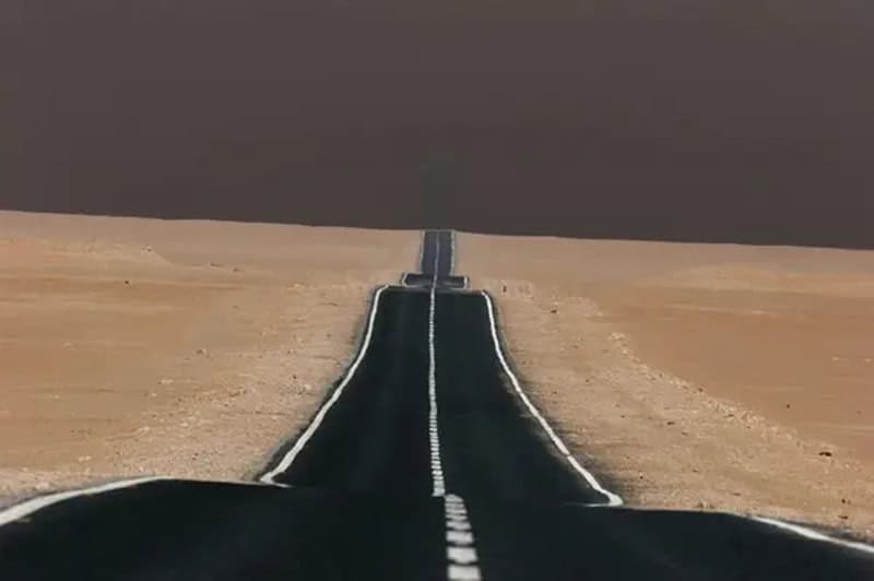 Long empty road stretching into a dark, cloudy sky in a barren landscape.