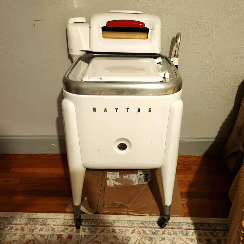 Vintage Maytag washing machine with a white body and metal accents, on a wooden floor.