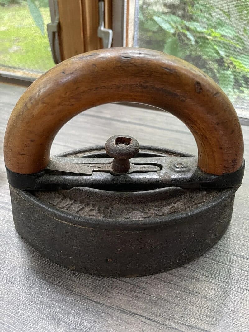 Vintage flat iron with wooden handle on a wooden surface.