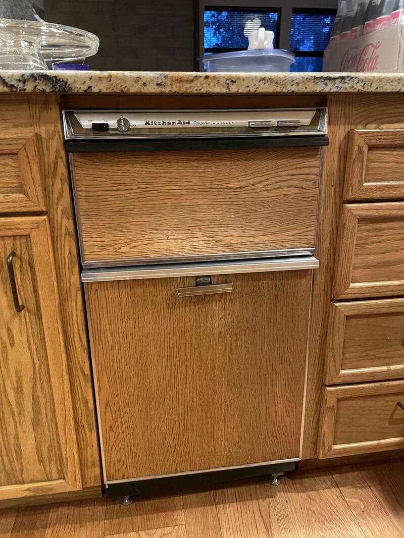Vintage KitchenAid dishwasher in wooden panel with surrounding cabinets.