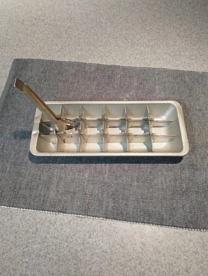 Vintage ice cube tray with metal tongs on a gray surface.
