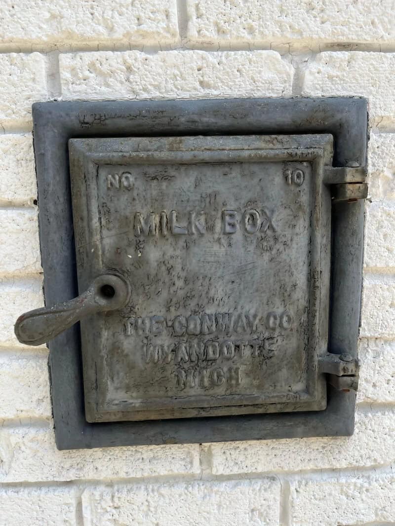 Vintage metal milk box attached to a white brick wall.
