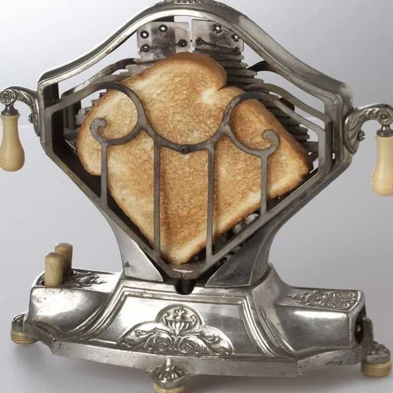Vintage bread toaster with toast inside, ornate metal design, cream-colored handles.
