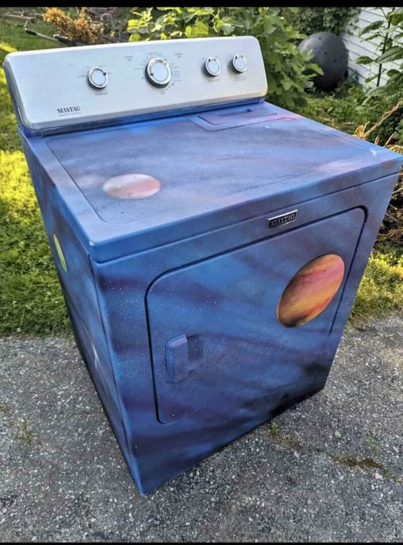 Washing machine with a space galaxy design, planets and stars on the exterior.