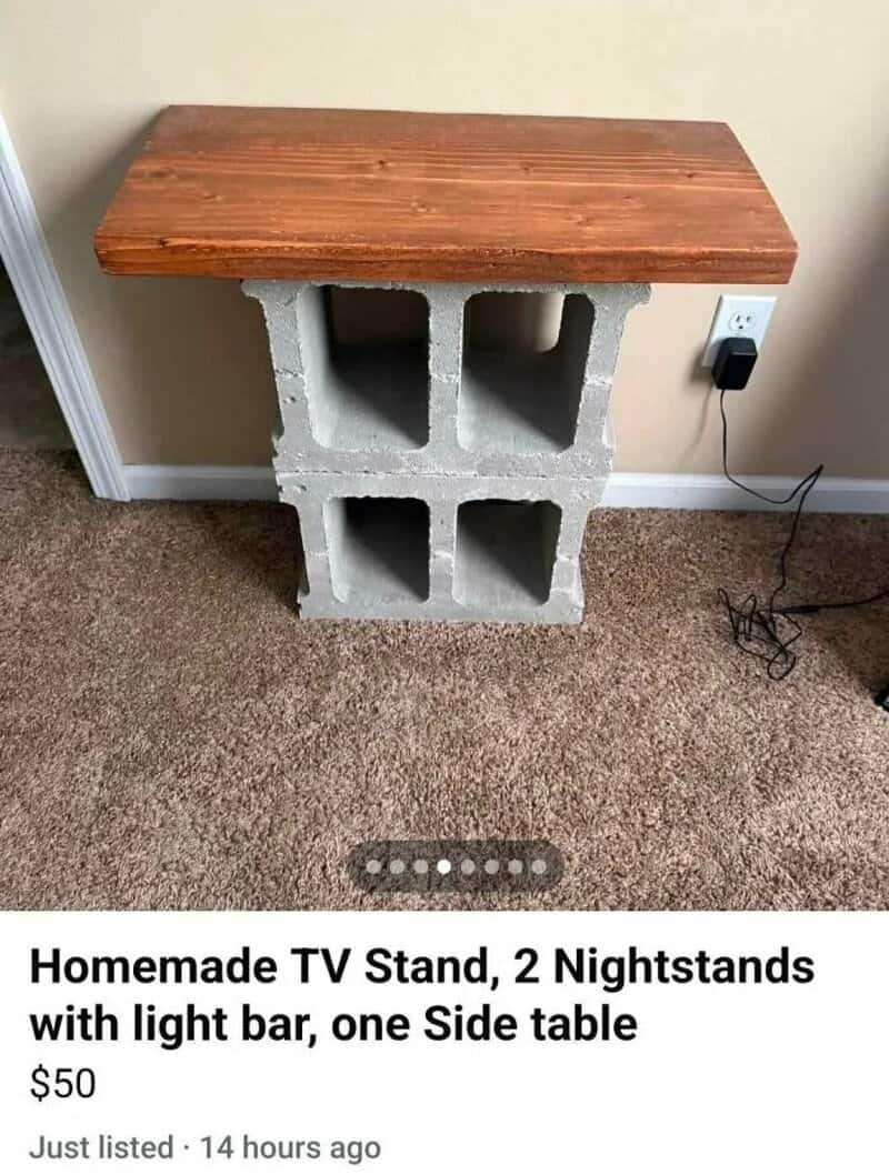 Homemade TV stand with cinder blocks and a wooden top, next to an electrical outlet.
