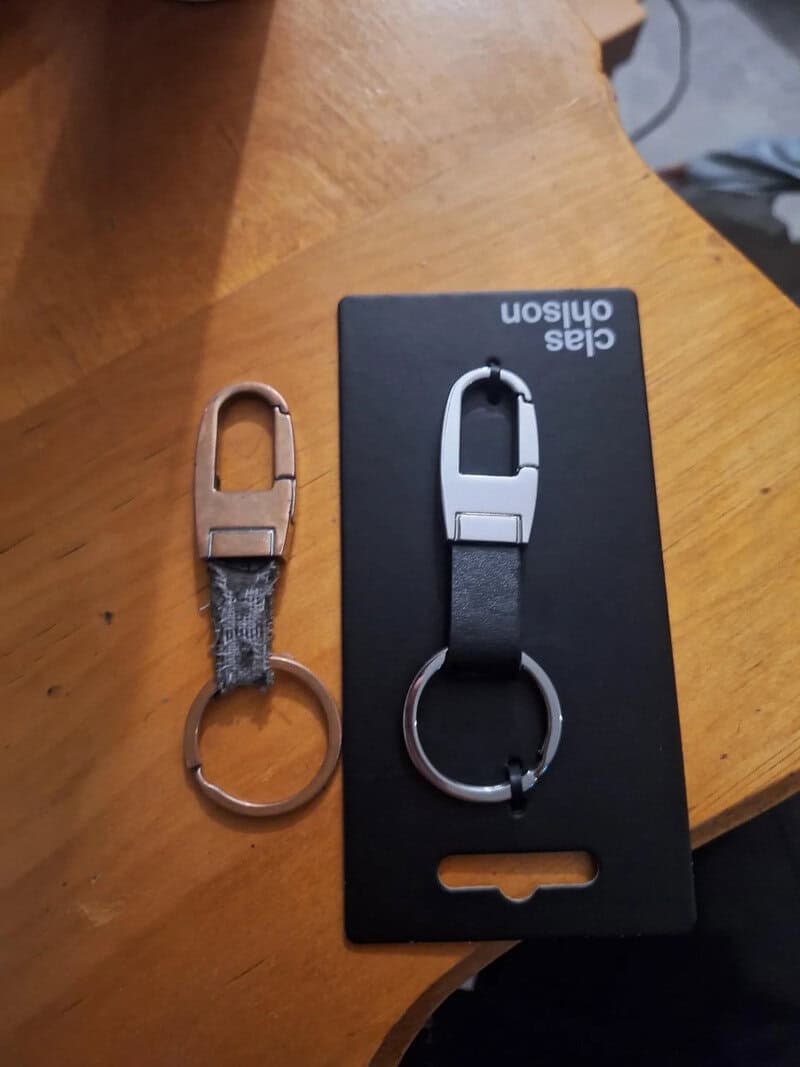 Two keychains, one new and one worn, on a wooden surface with a Calas Olhson box.