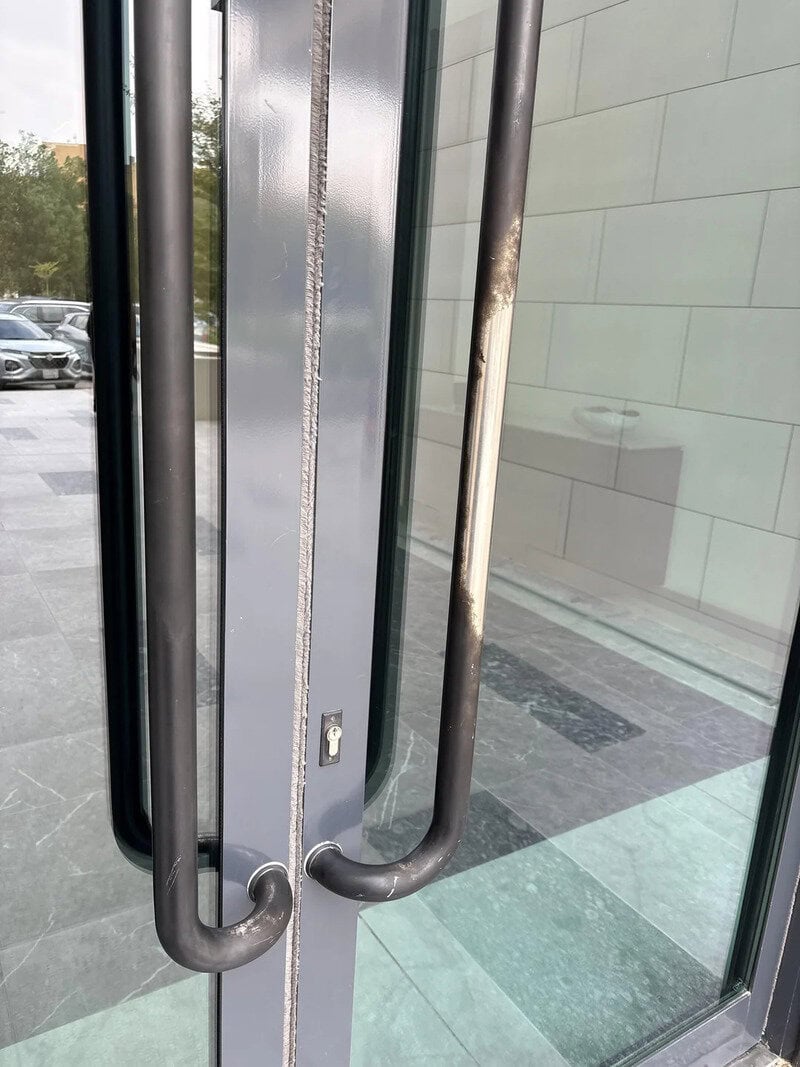 Close-up of a metal door handle with a chain lock on a glass door.