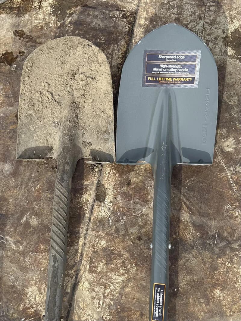 Old and new shovels placed on a stone surface.