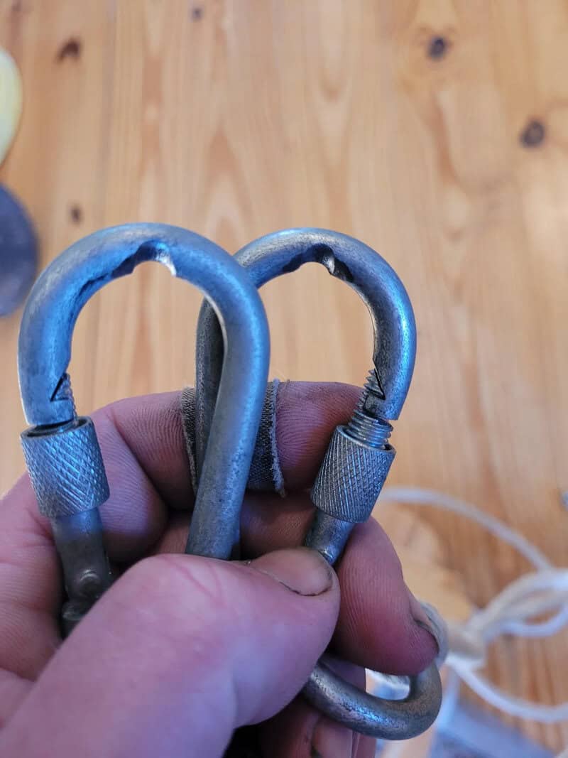 Close-up of a hand holding three metal carabiners against a wooden background.