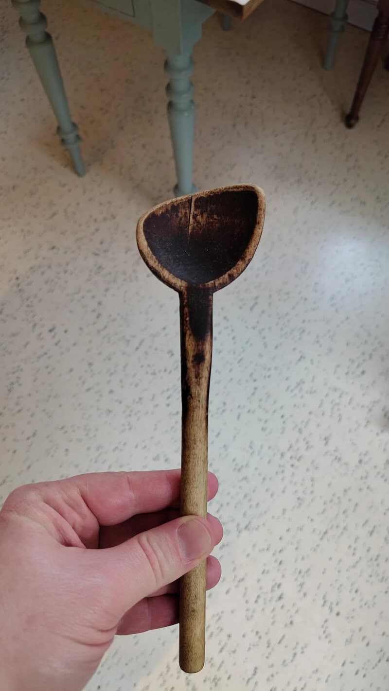 Hand holding a small, worn wooden scoop with a darkened bowl.