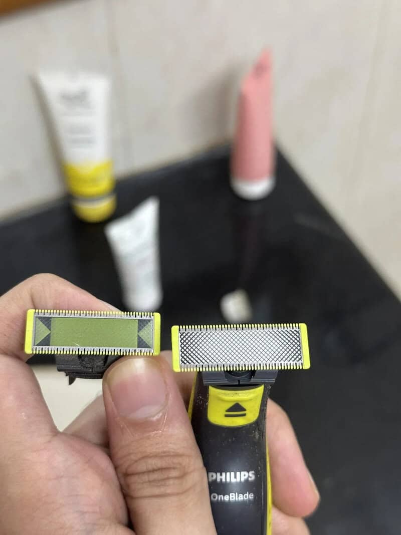 Close-up of a hand holding a Philips OneBlade razor with a yellow and black handle.