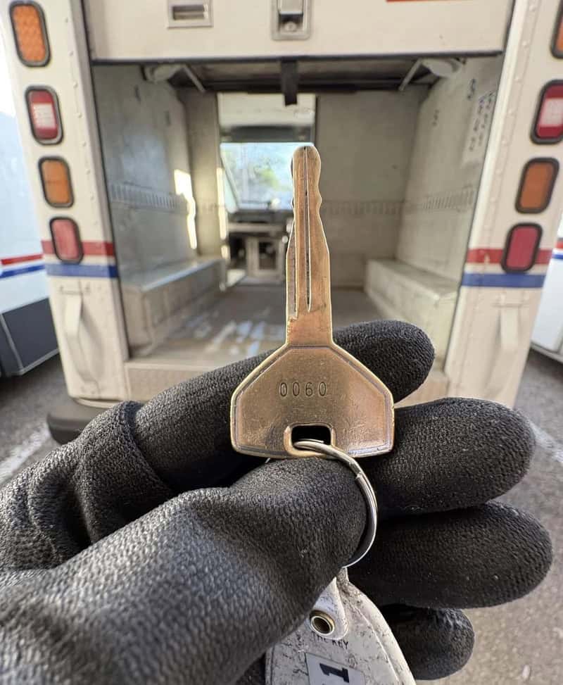 Close-up of a hand in a black glove holding a key in front of an ambulance.