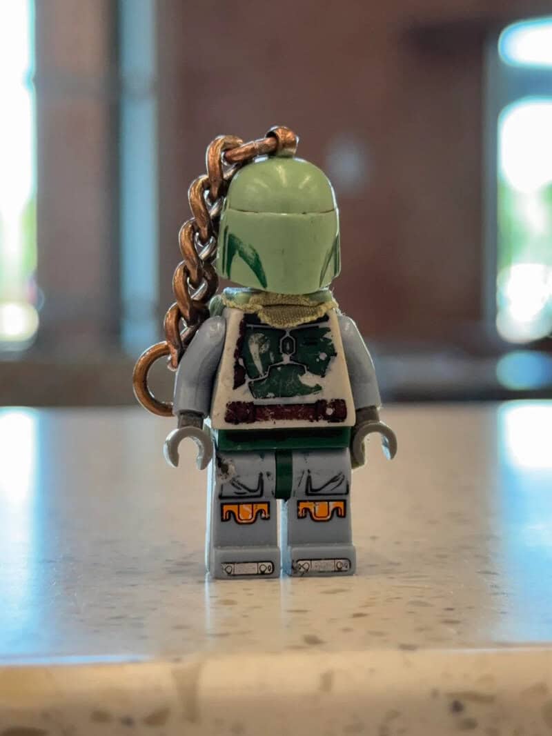 Lego minifigure with green helmet, gray outfit, and chain on back, standing on a surface.