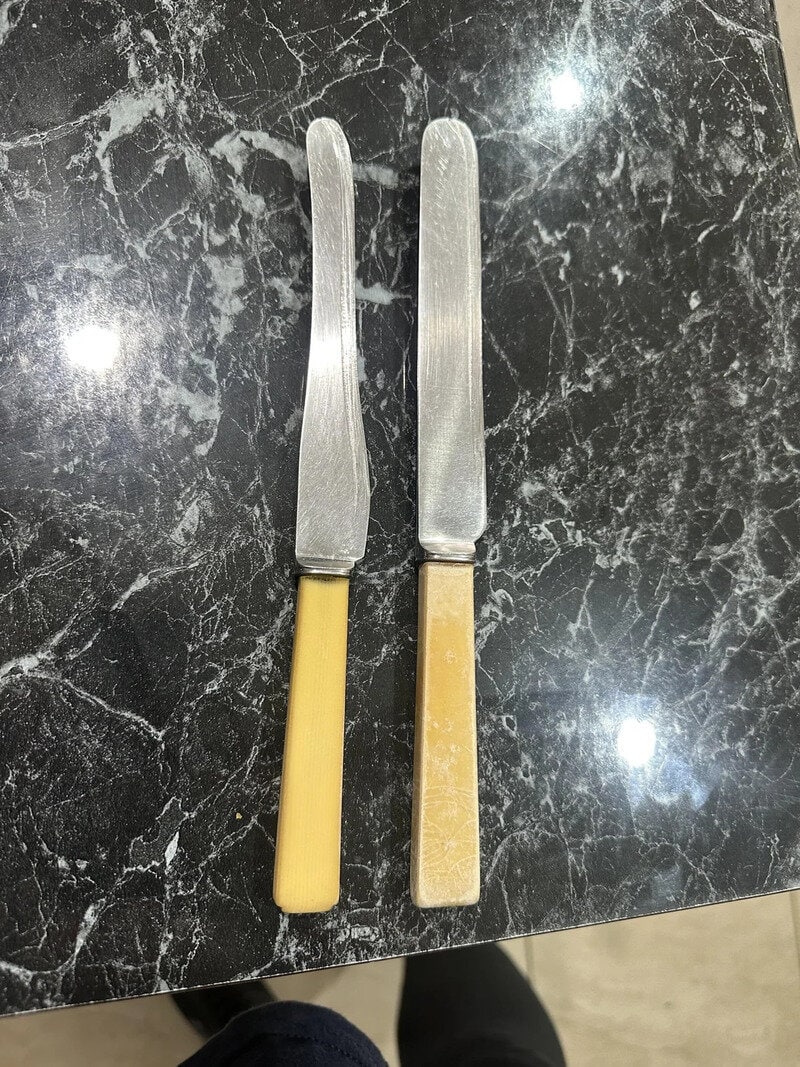 Two butter knives with yellow and beige handles on a black marble surface.