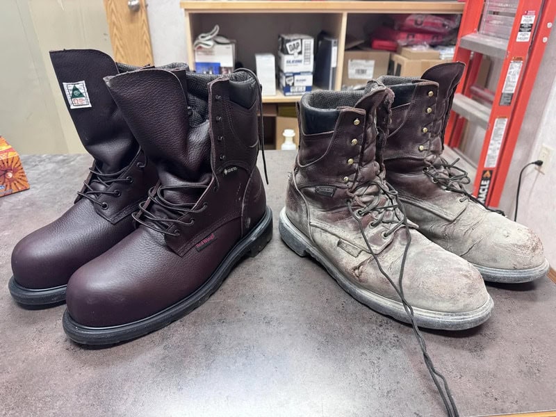 Two pairs of work boots, one new and one old, on a table in a workshop.