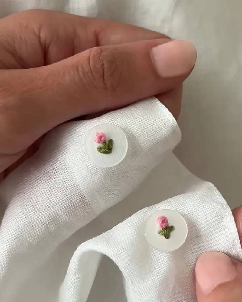 Close-up of two white fabric pieces with pink and green embroidered buttons.