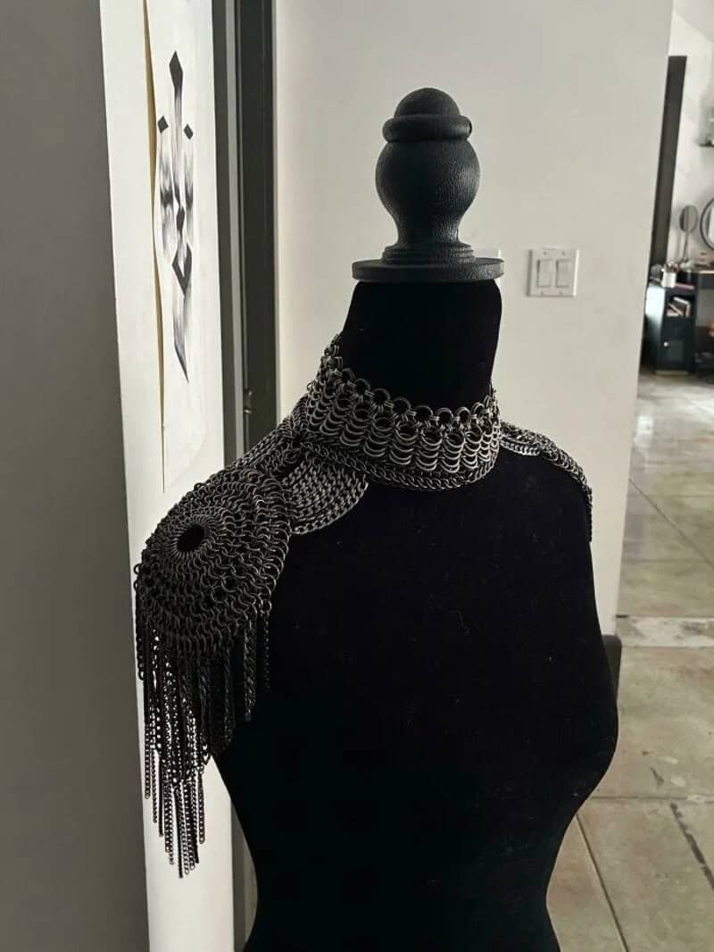 Black mannequin with a silver chain shoulder accessory in a craft store.