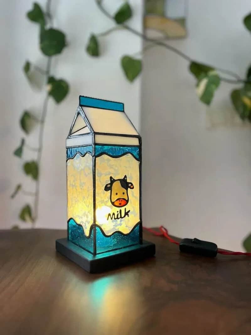 Colorful LED lamp shaped like a milk carton with a cow illustration, on a wooden surface.