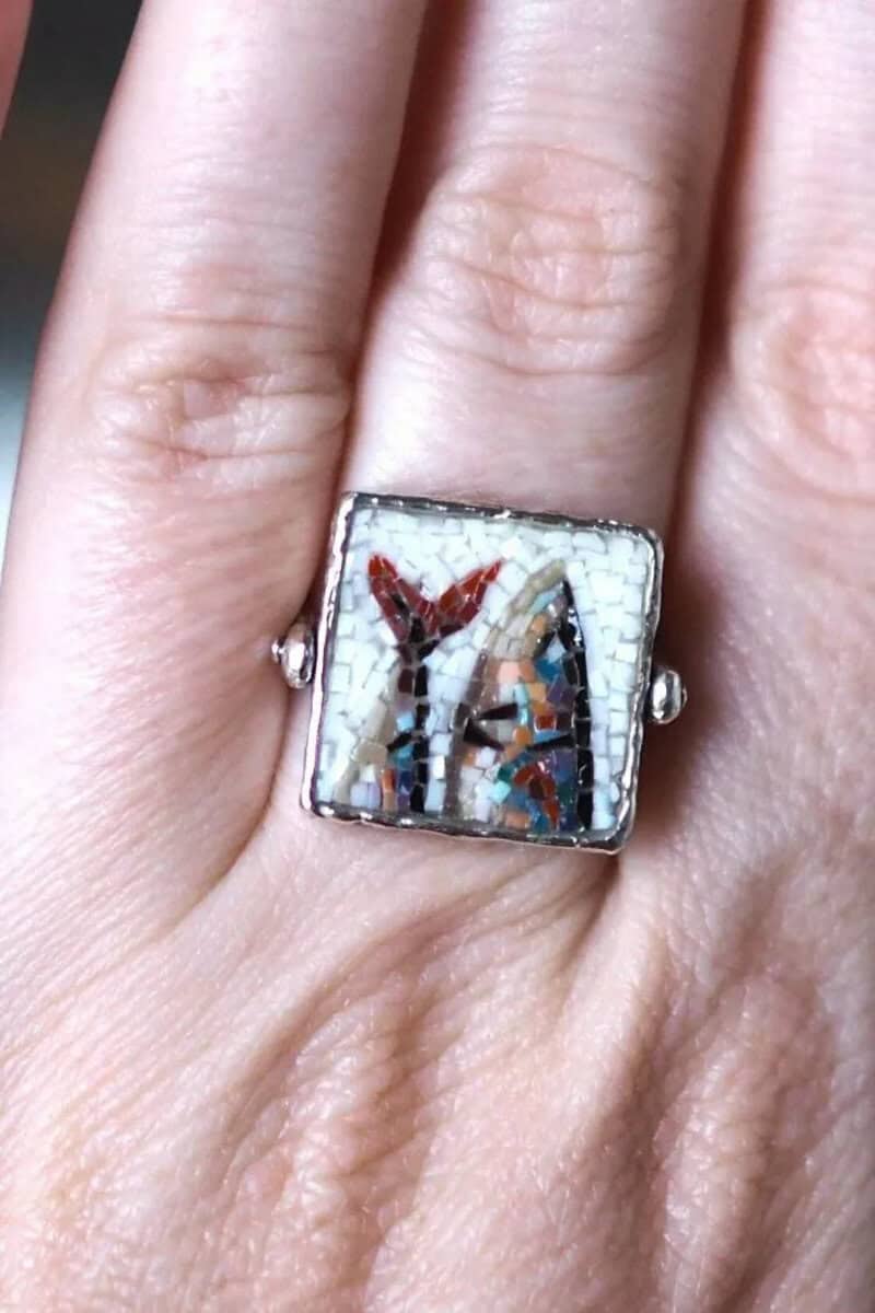 Close-up of a mosaic ring with a colorful butterfly design on a finger.