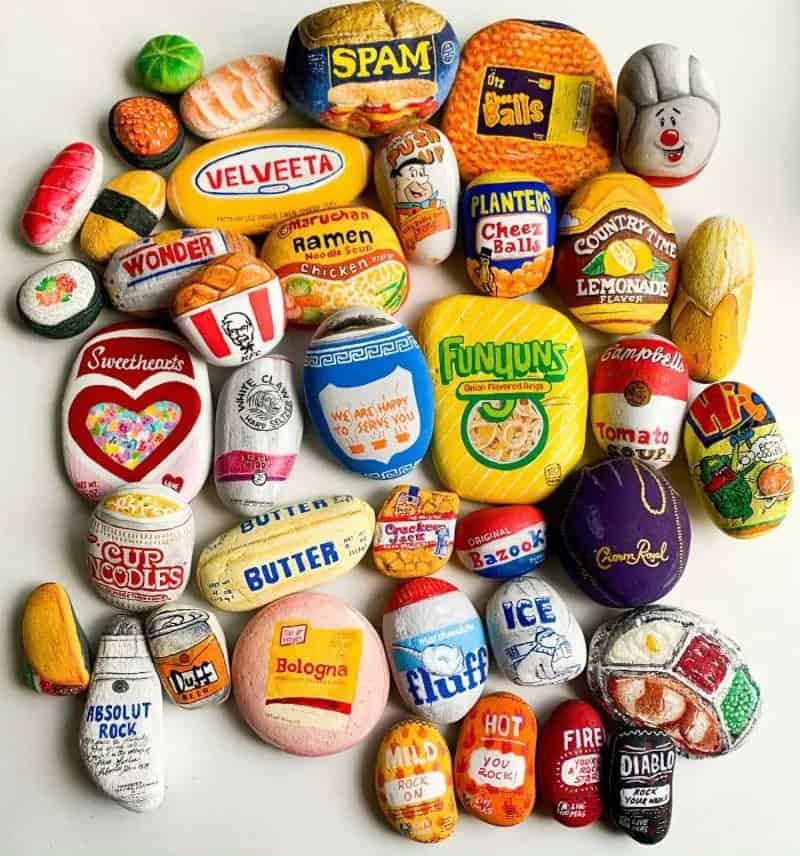 Collection of painted rocks with various food and brand designs, including Spam, Velveeta, Wonder, R.