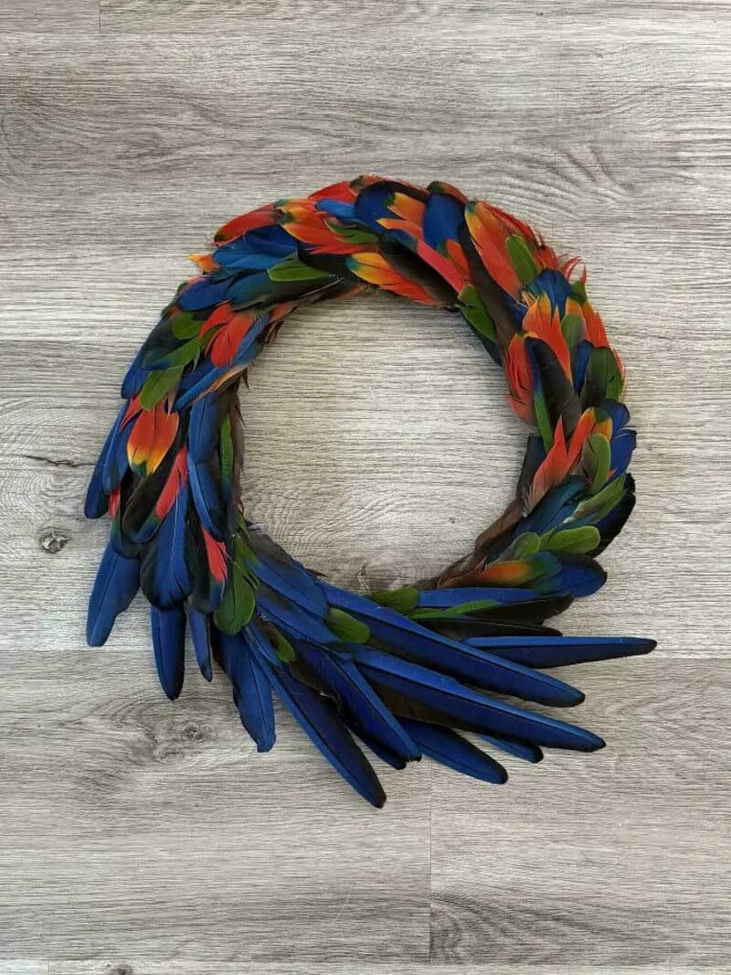Colorful feather necklace with red, blue, green, and orange feathers on a gray wooden surface.