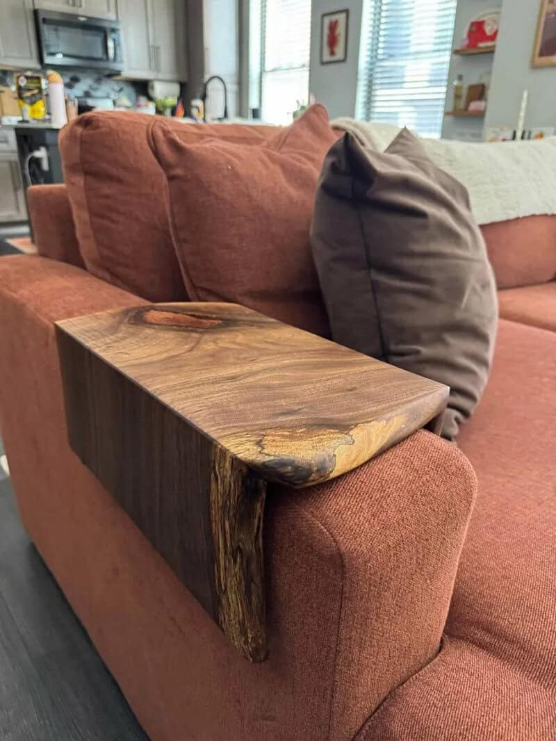 Close-up of a wooden armrest on a rust-colored sofa in a living room.