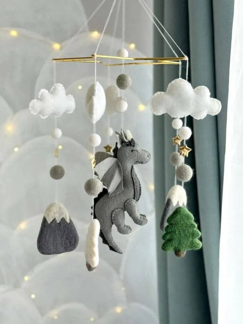 Felt baby mobile with clouds, mountains, tree, and unicorn, hanging near window.