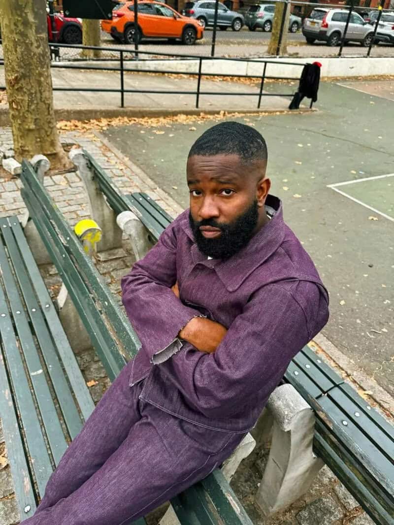 Man with beard in purple denim outfit sitting on park bench.
